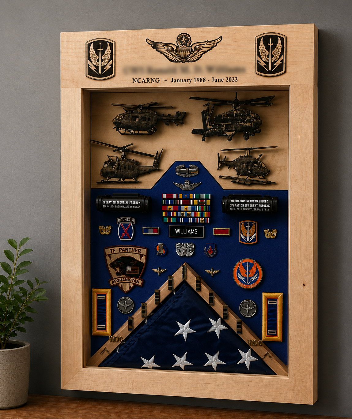 Military shadow box display with model helicopters, military patches, medals, ribbons, and a folded American flag honoring service members.