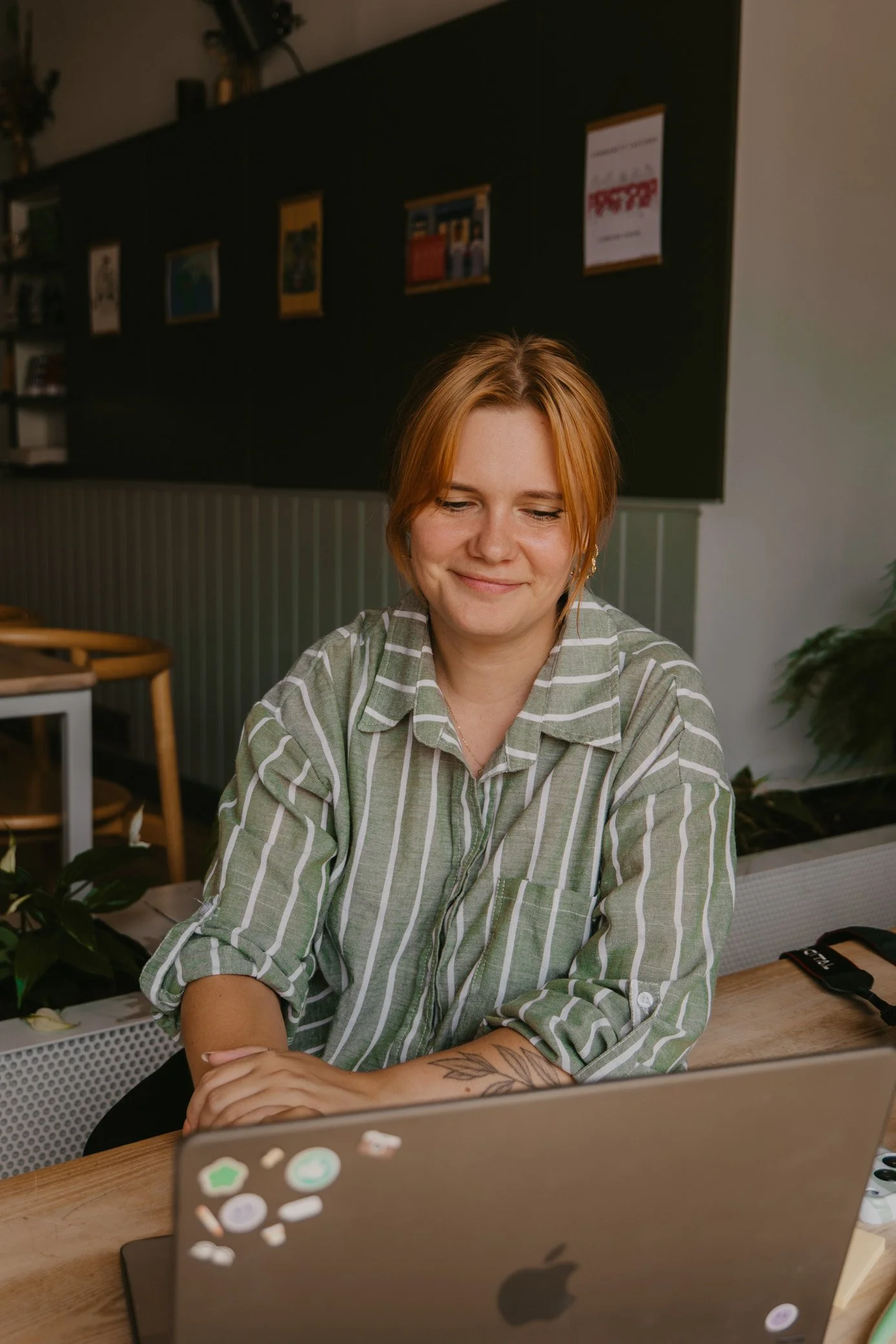 Monthly social media management for Cornwall small businesses. Leah Croft smiling while sitting at a table, working on a laptop in a cosy, modern room with framed pictures on the black wall behind her.