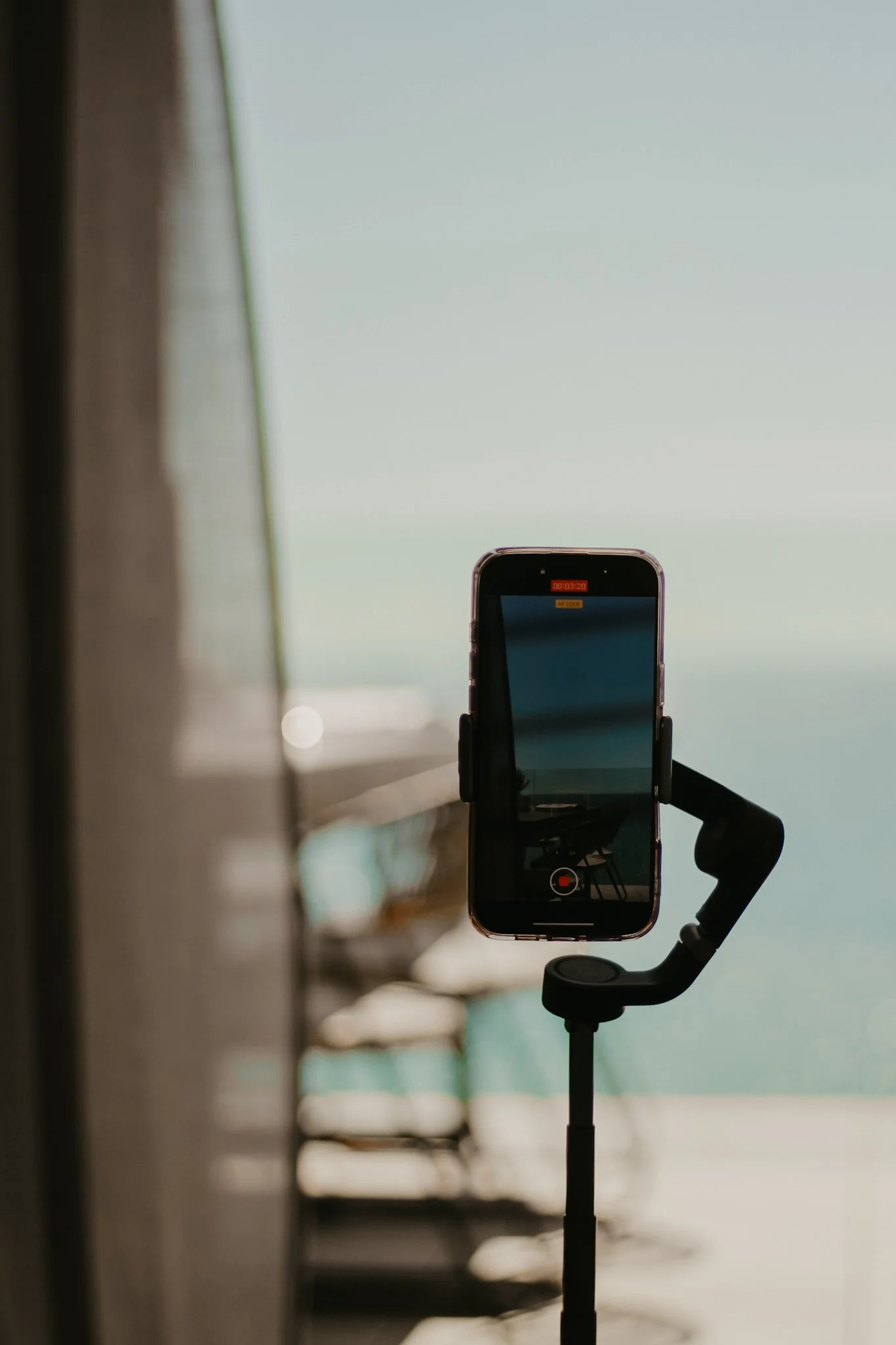 Smartphone mounted on a stabilizer recording video, with a blurred boardwalk and ocean in the background.