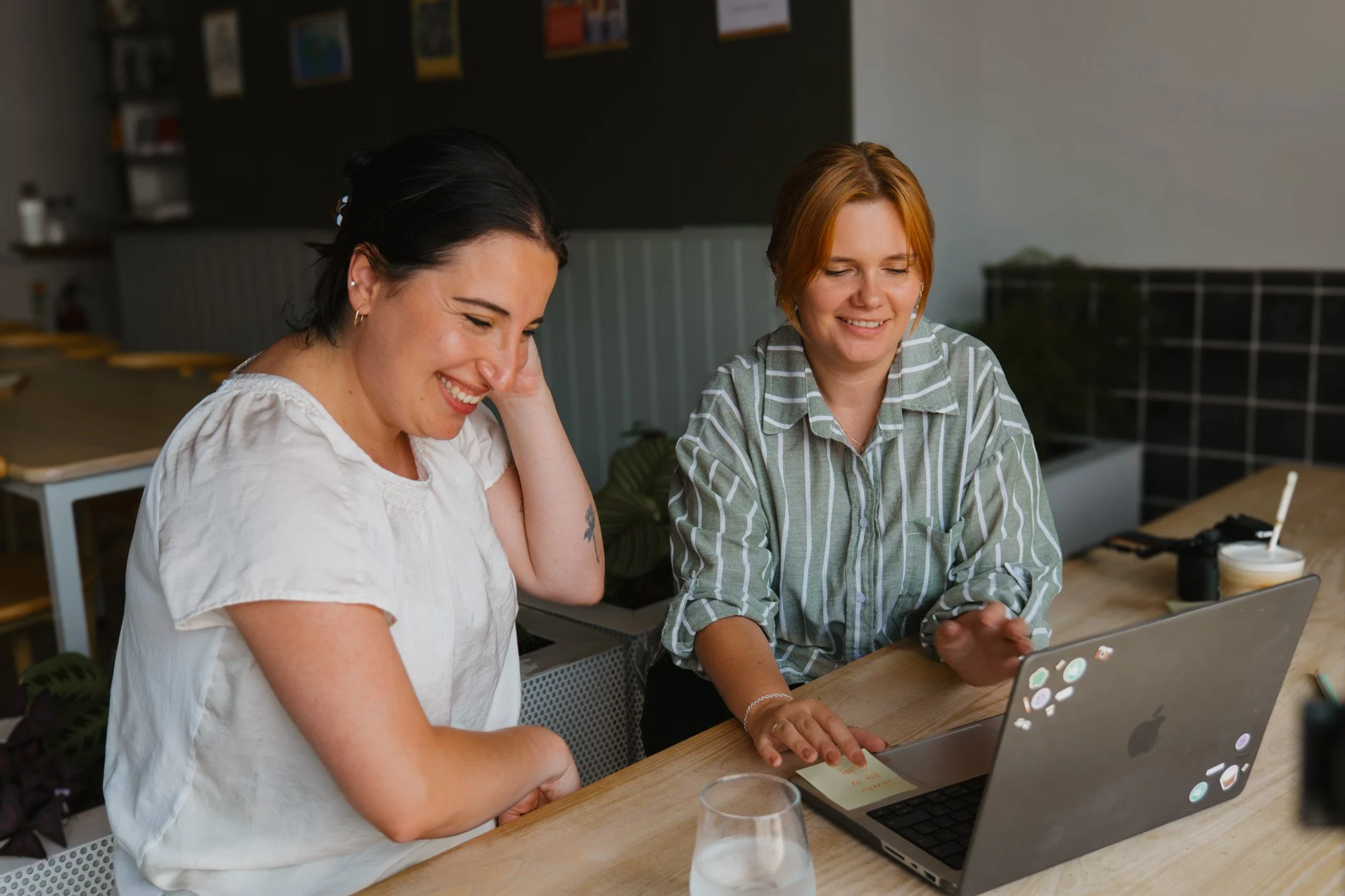 Leah and a client, 1:1 social media training in Cornwall, looking at a laptop with smiley stickers, sharing a moment of laughter in a casual indoor setting.