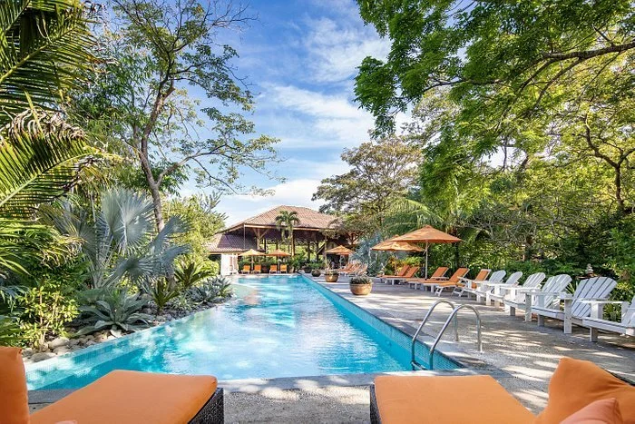Outdoor pool area with lounge chairs, umbrellas, and tropical greenery at a resort