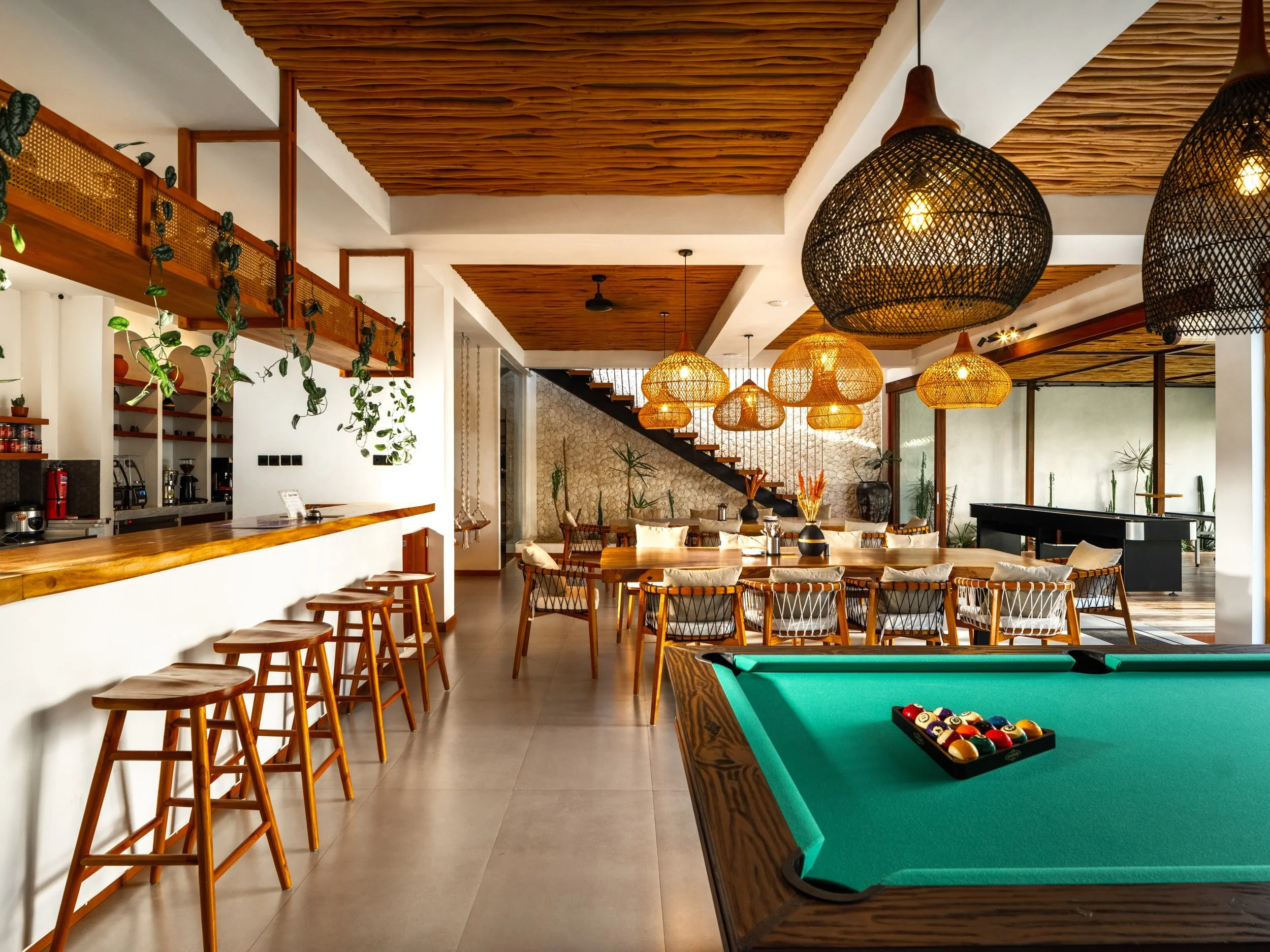 Interior of a modern lounge or game room with pool table, hanging pendant lights, wooden ceiling, and seating area.
