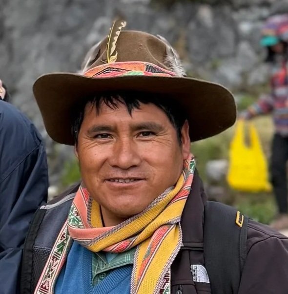 Man wearing a wide-brimmed hat, colorful scarf, and backpack smiling outdoors.