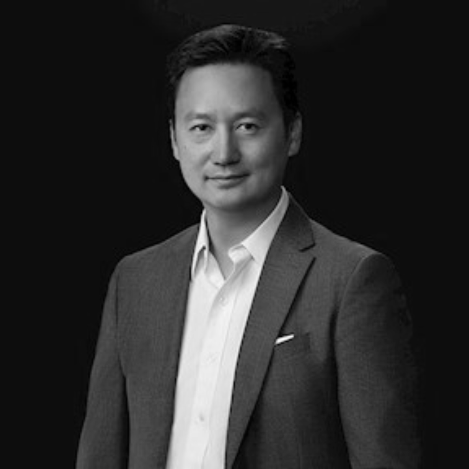 Black and white portrait of an Asian man in a suit and white shirt against a dark background.