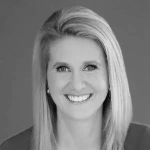 A black and white professional headshot of a woman with shoulder-length blonde hair, smiling at the camera.
