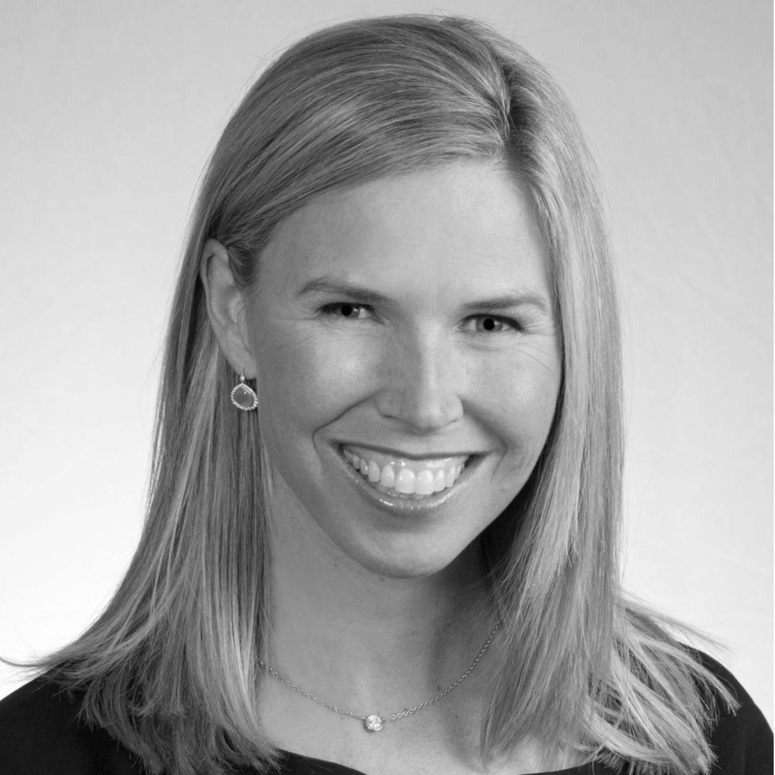 Black and white portrait of a woman smiling, with straight hair, wearing earrings and a necklace.