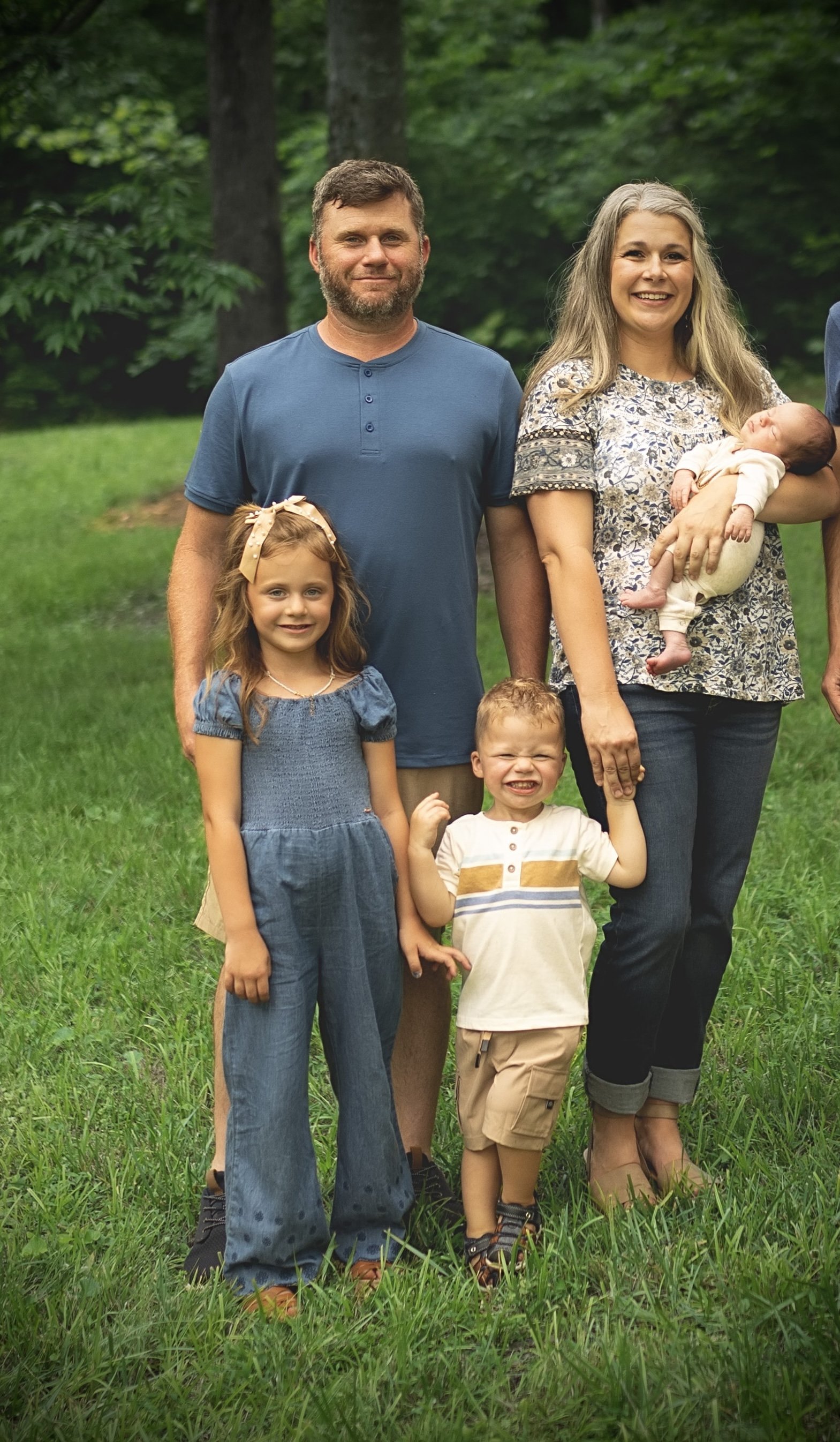 A happy family in their yard with lush green grass and trees, including a man, a woman holding a baby, and two young children.