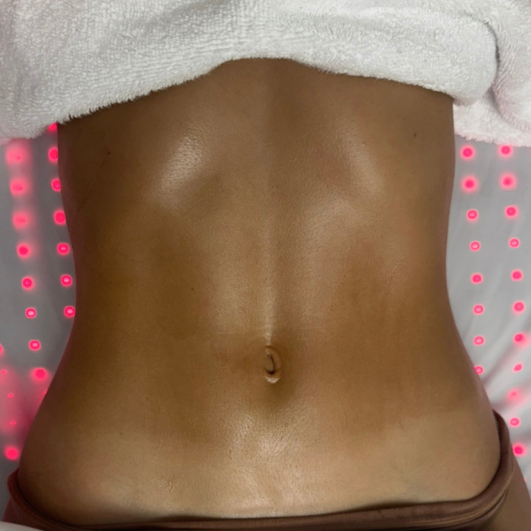 Close-up of a person's bare midsection with smooth, tan skin and a visible navel, partially covered by a white towel, with red and gray LED lights in the background.