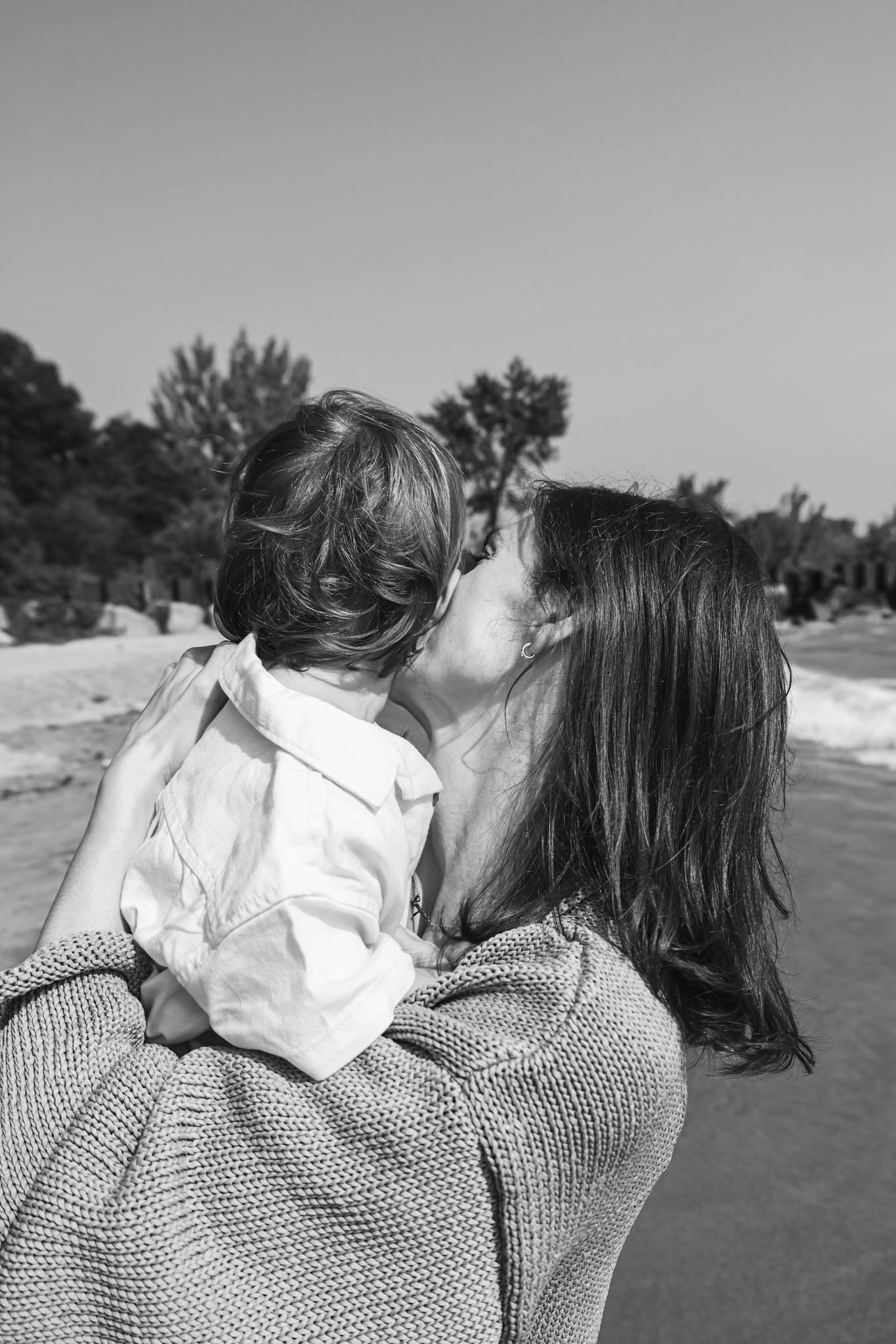 Carli holding and kissing her young son at the beach.