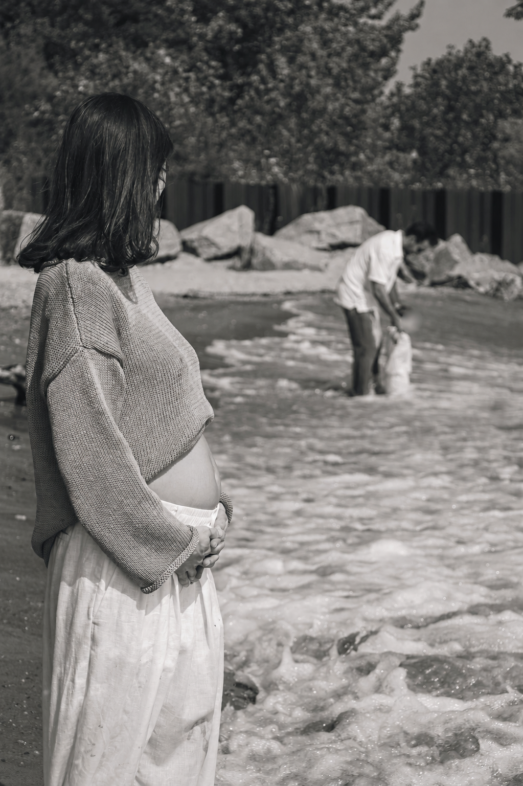 Pregnant mother standing at the beach with her family in the background.