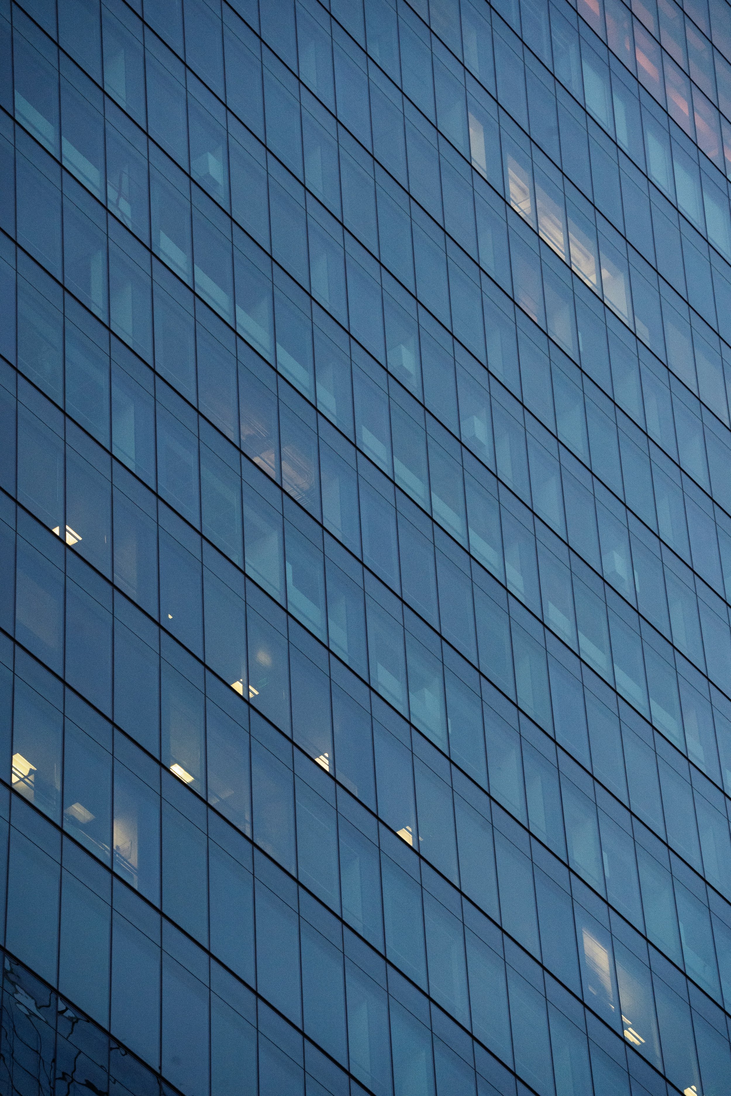 Close-up of a modern glass office building reflecting the sky, with visible illuminated and dark office windows.