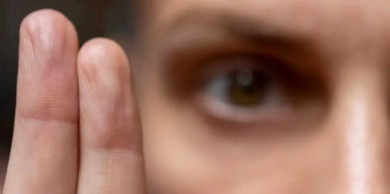 A person close to their face holding two fingers up near their eye.
