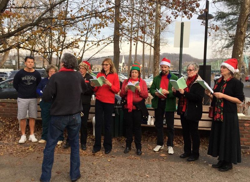 People singing Christmas carols outdoors with holiday attire such as Santa hats and Christmas sweaters.
