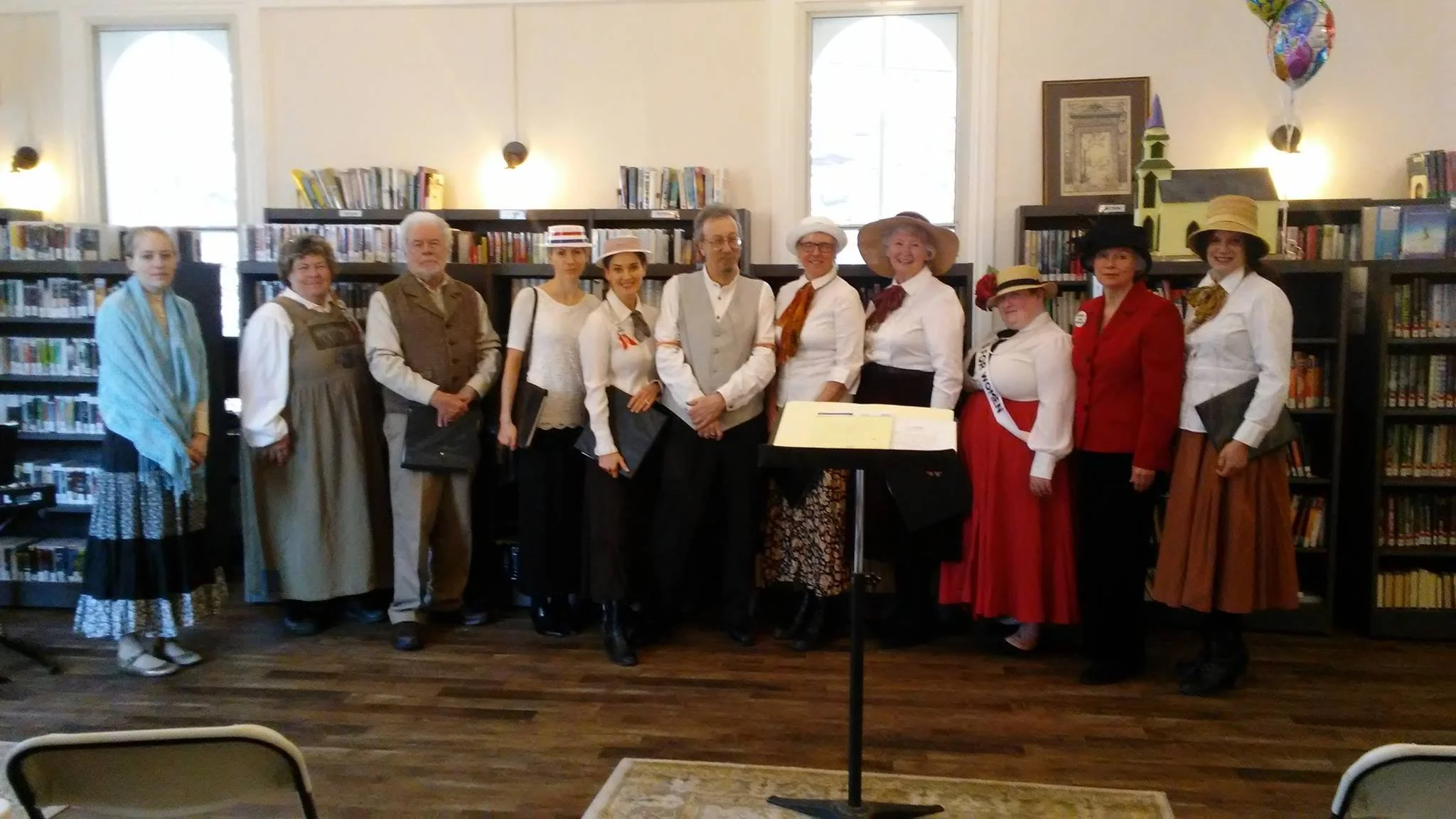 People dressed in historical costumes standing in a library, posing for a photo.