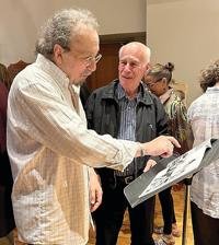Two elderly men looking at and discussing a framed picture or document at an indoor social event.