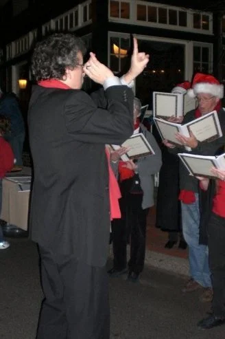 A choir or singing group performing outdoors at night, with a conductor leading them.