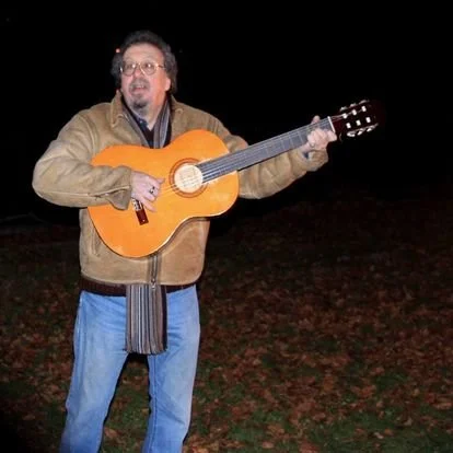 Man playing an acoustic guitar outdoors at night.