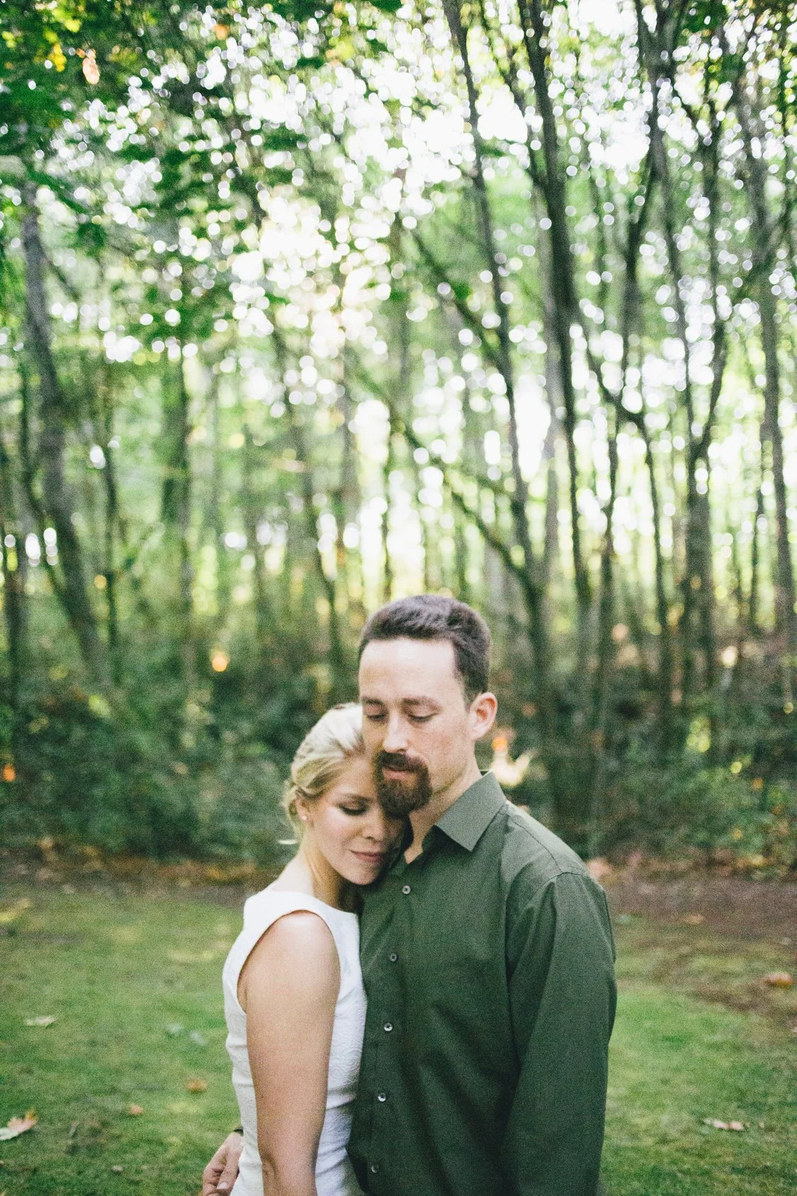 A couple embracing in a forest, with trees and sunlight in the background.