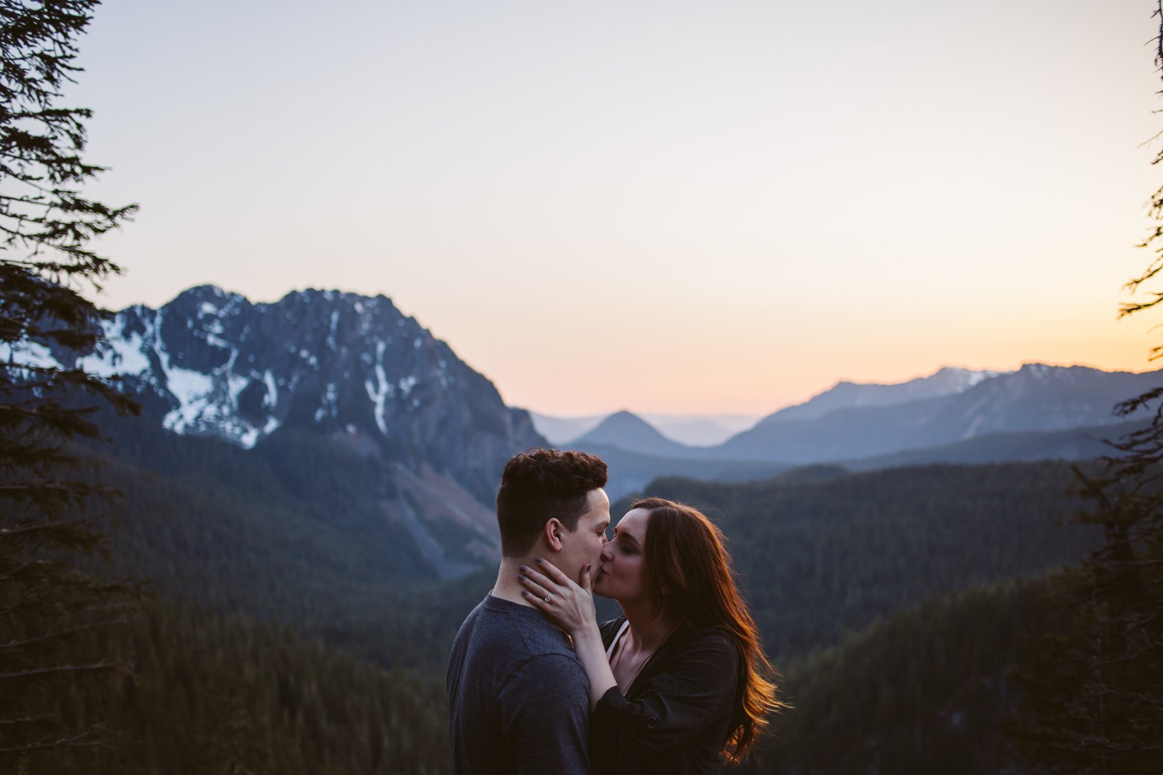 A couple kissing in front of mountains at sunset.