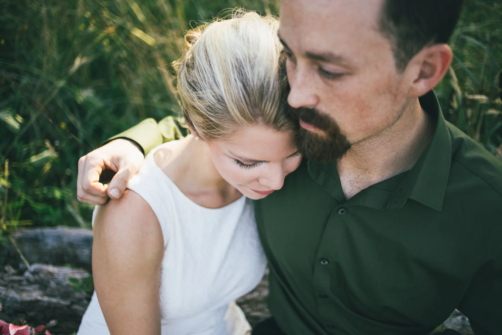 A man and a young girl are sharing a close, tender moment outdoors with green foliage in the background. They have their heads touching and eyes closed, showing an emotional connection.