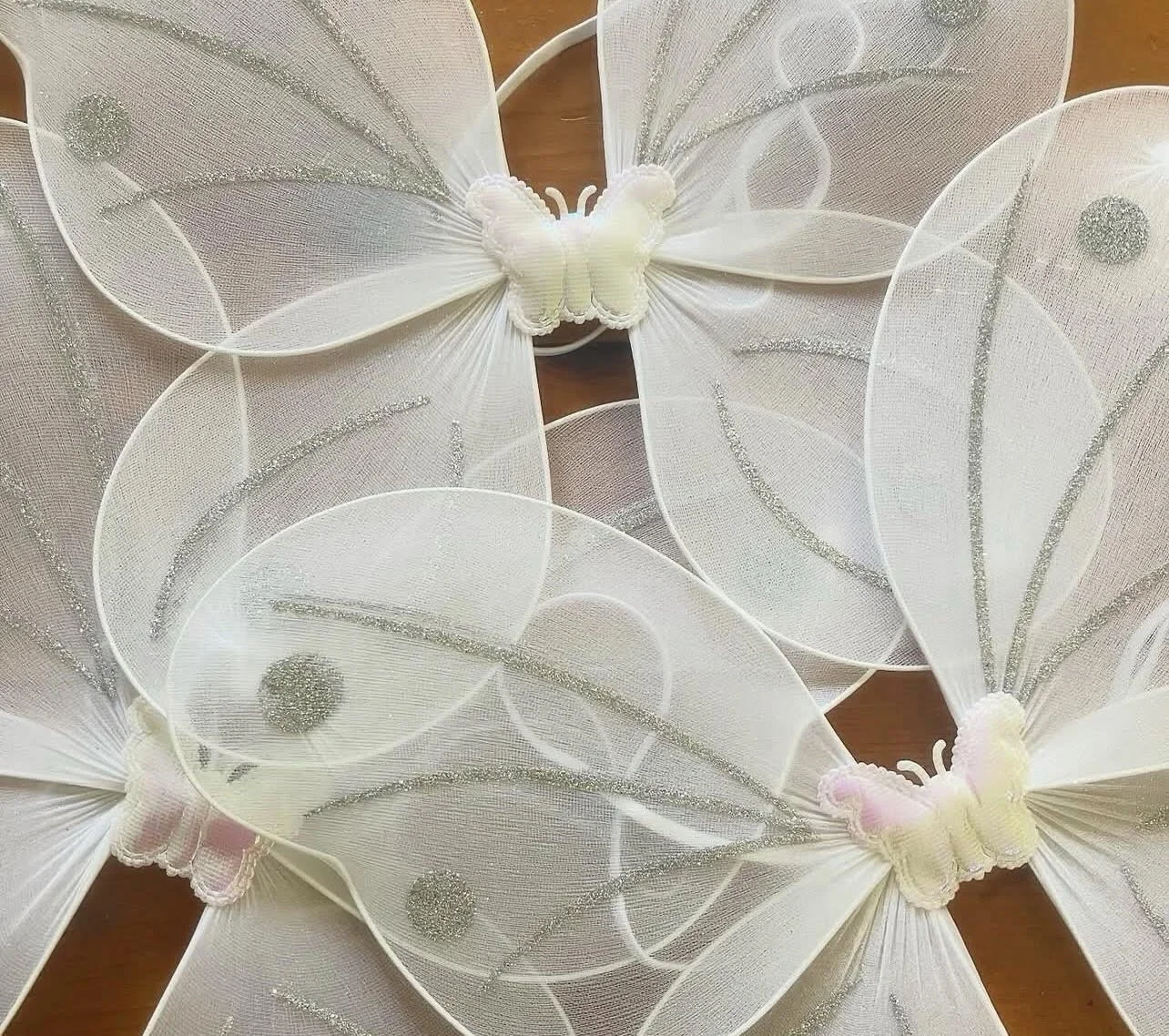 White butterfly-shaped decorative wall hanging with silver glitter accents, featuring a central butterfly and fabric wings with curved lines and circles, lying on a wooden surface.