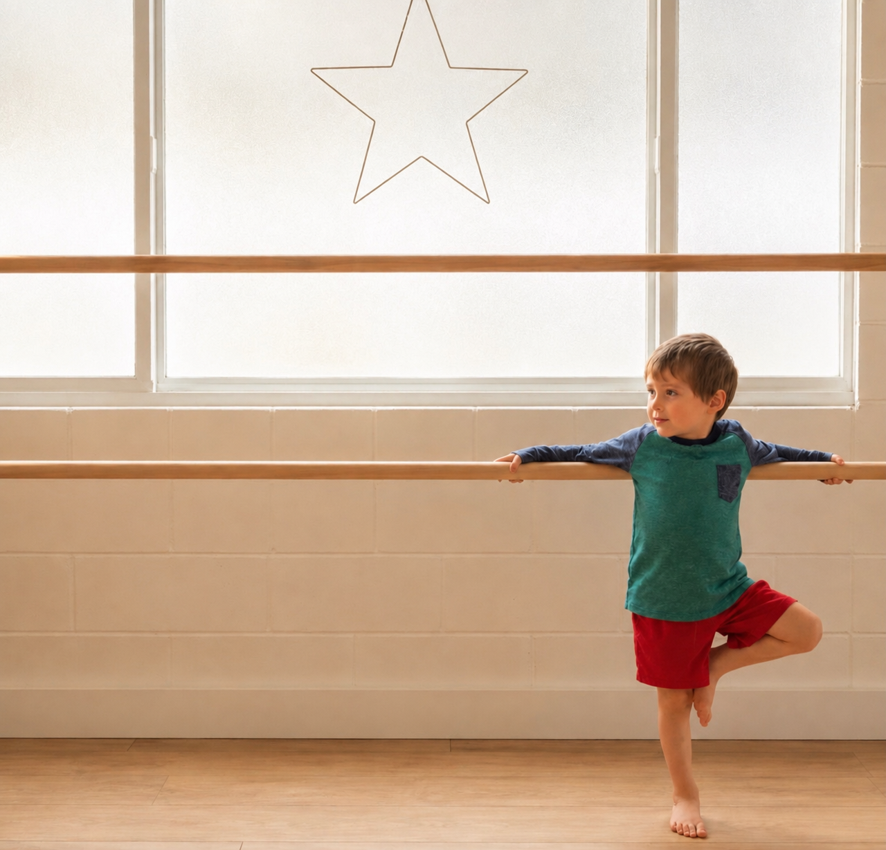A young boy practicing ballet at a dance studio, standing on one foot with arms outstretched on a ballet barre, with a star-shaped decoration on the window in the background.