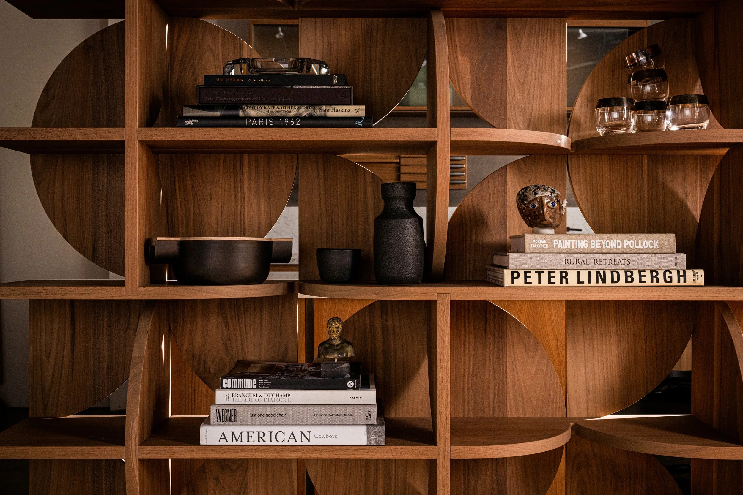 A wooden bookshelf with various books, decorative objects, and glasses arranged in a grid pattern.