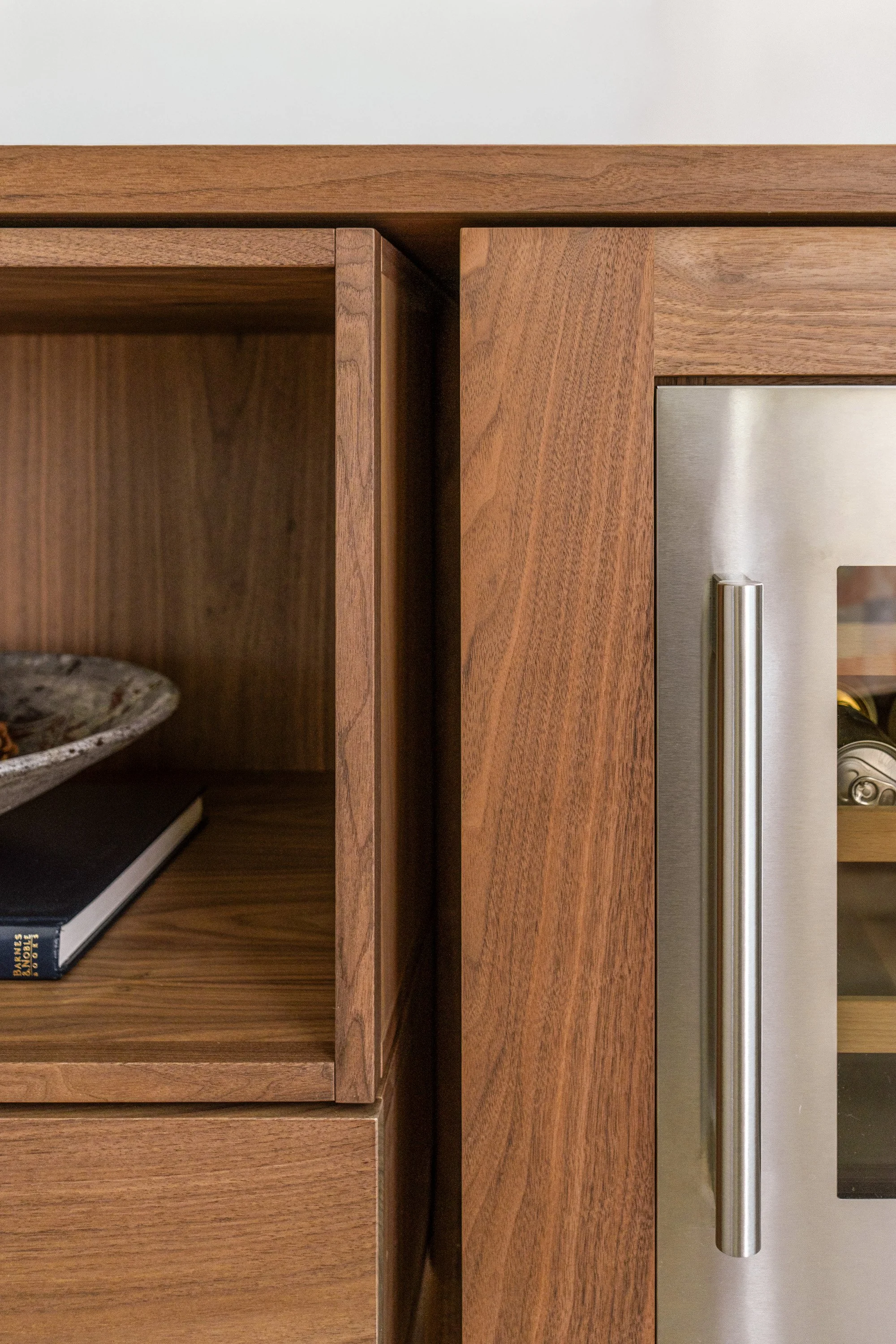 Close-up of a wooden cabinet with a stainless steel handle, a shelf with a book, a plate, and a smartphone inside.