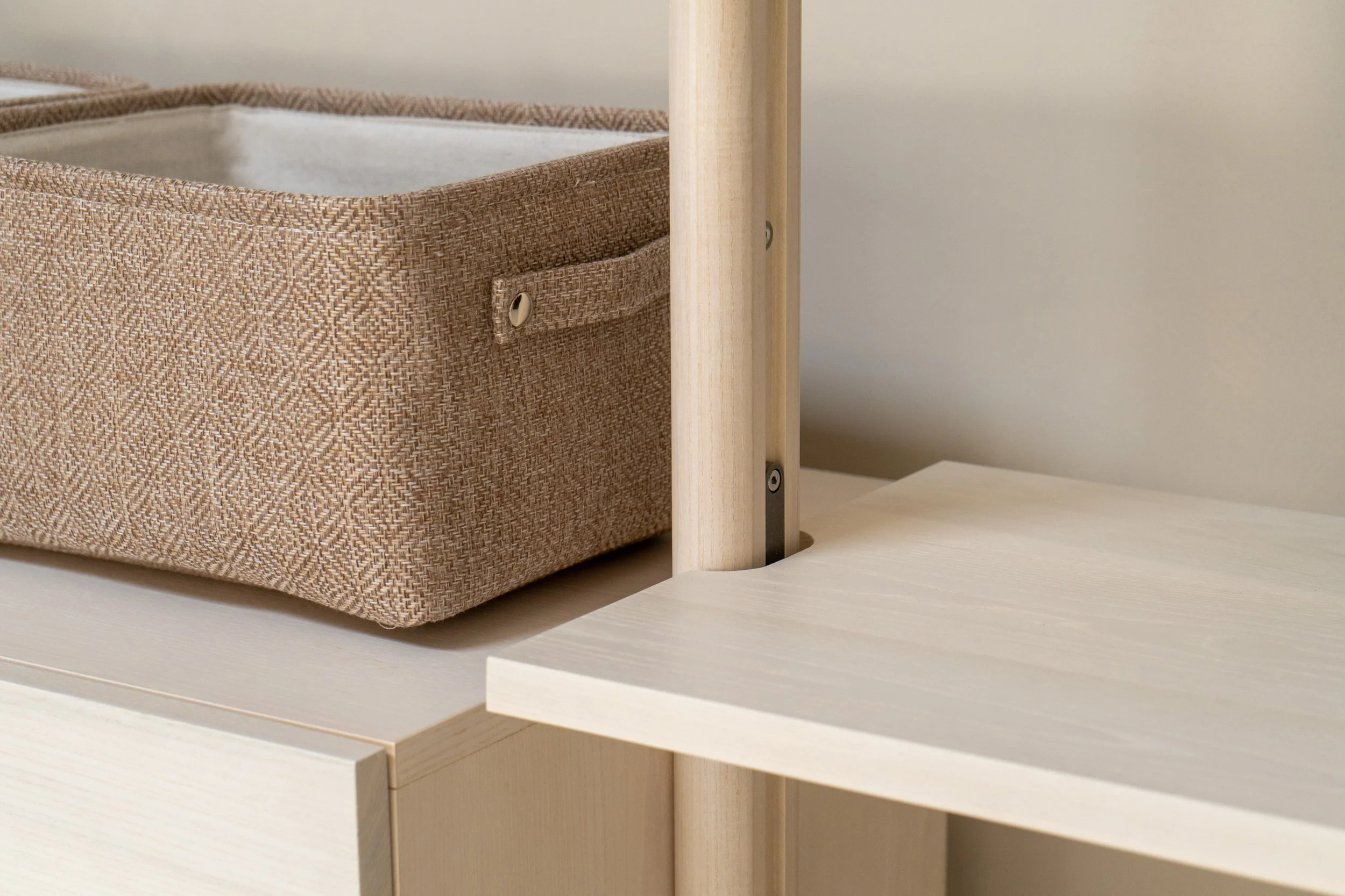 Close-up of a beige fabric storage bin with a small handle, placed on a light-colored wooden shelf.