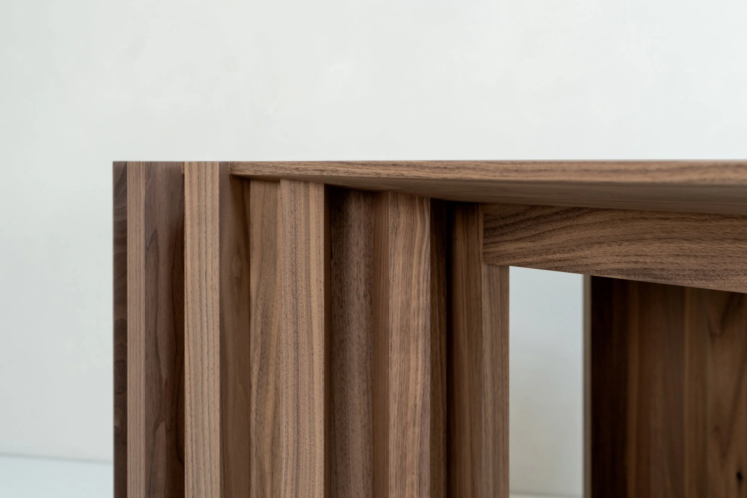 Close-up of a wooden piece with vertical and horizontal slats, showcasing natural wood grain on a plain white background.