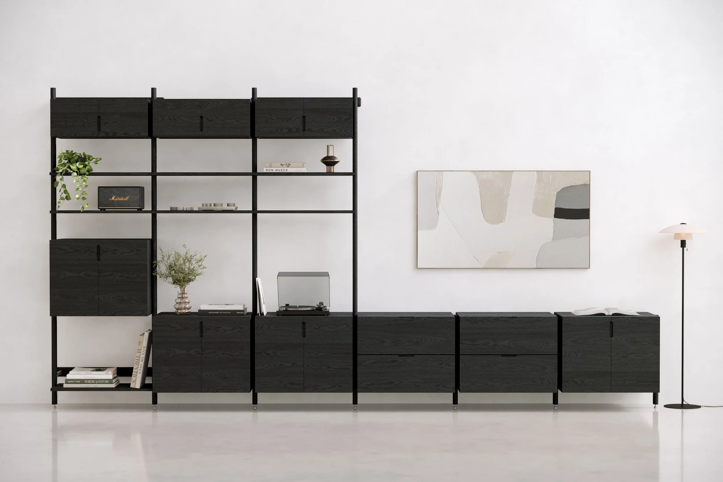 Modern black shelving unit against a white wall with books, a plant, a lamp, and decorative items, with a large abstract art piece on the right, and a floor lamp on the far right.