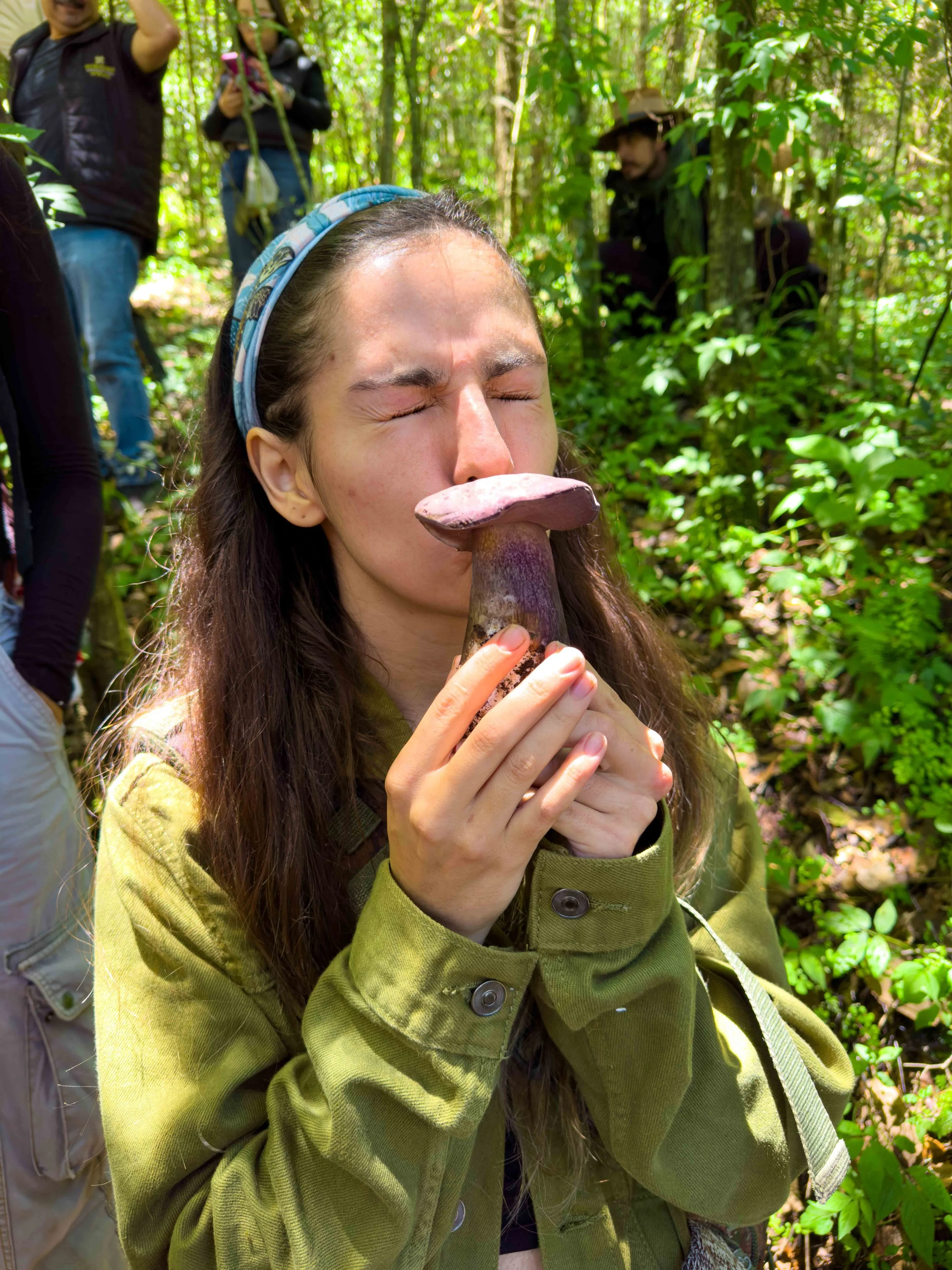 Mujer con sudadera verde sosteniendo un hongo en un bosque.