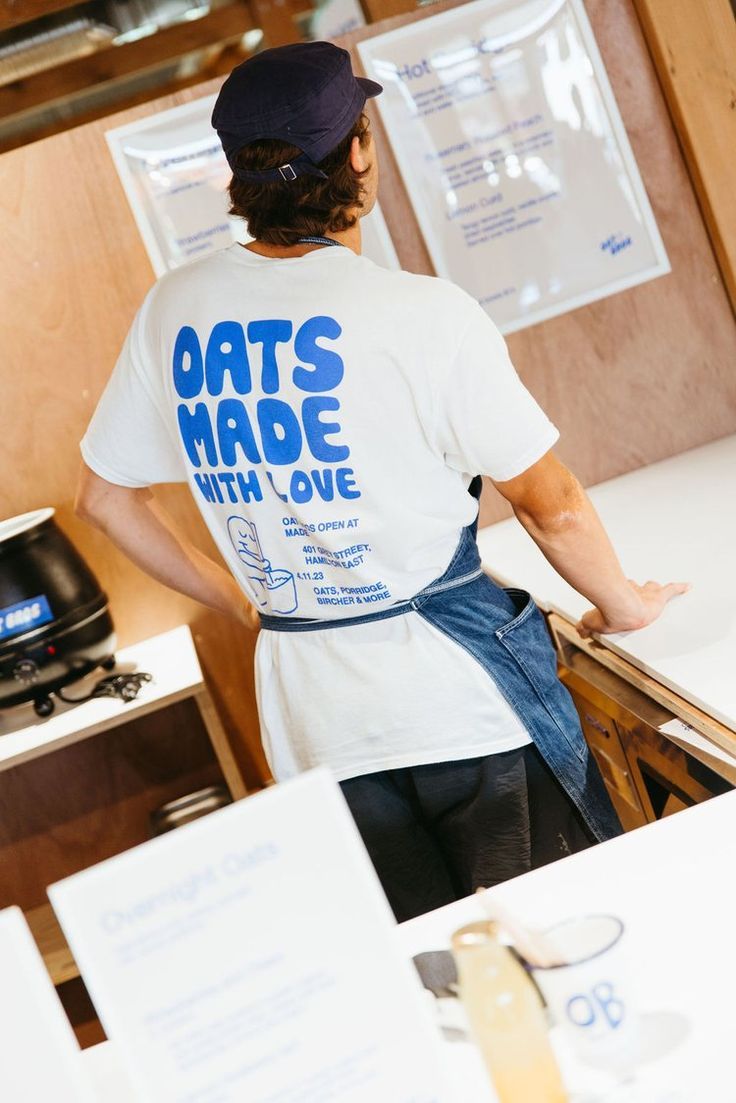 Persona de espaldas en una cafetería, llevando una camiseta blanca con diseño impreso en azul.