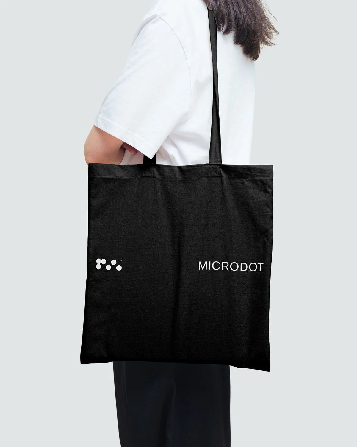 Bolsa negra personalizada para empresa con diseño de logotipo impreso en color blanco, sostenida por una persona como ejemplo de producto promocional corporativo.