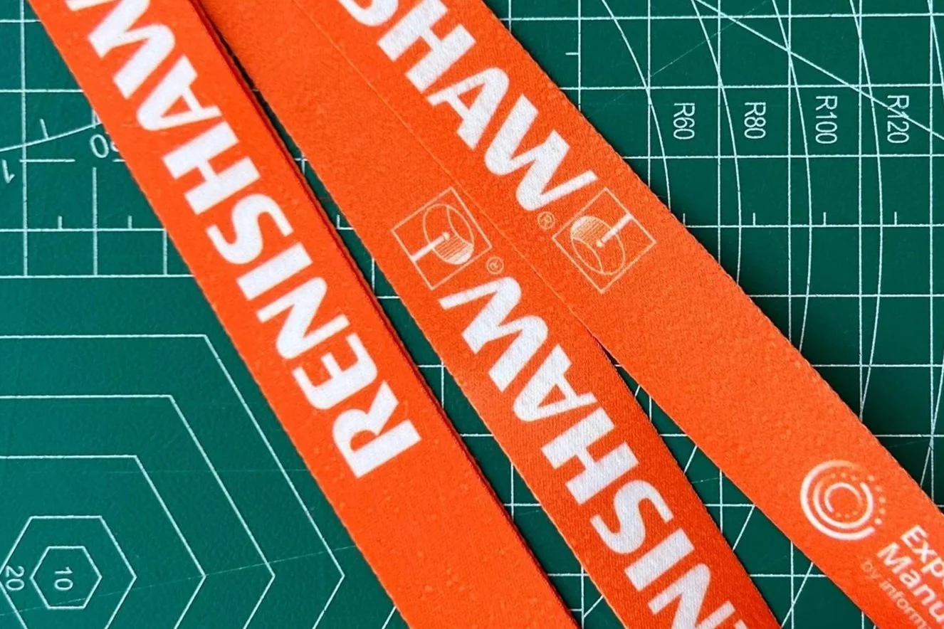 Detalle de lanyard personalizado para eventos con impresión de logotipo y texto de marca en cinta naranja, mostrando la calidad de impresión y acabado del producto.