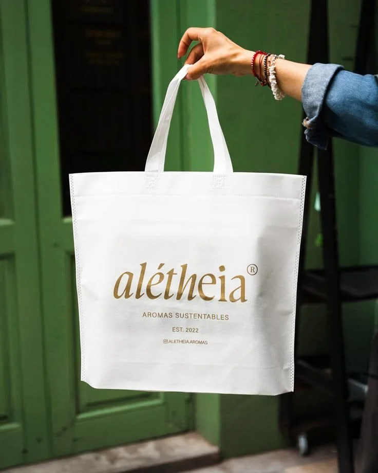 Bolsa ecológica de tela non woven personalizada con impresión de marca sustentable, mostrando logotipo y diseño gráfico sobre tela blanca.