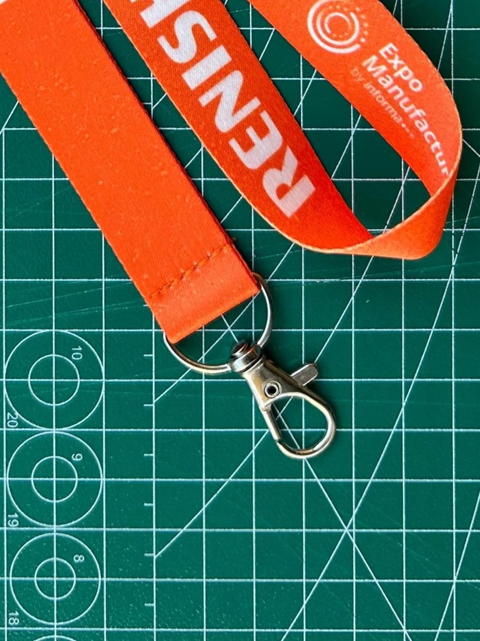 Lanyard personalizado para eventos con logotipo y texto impreso, equipado con gancho metálico tipo perico sobre una superficie de trabajo, mostrando detalles de fabricación.