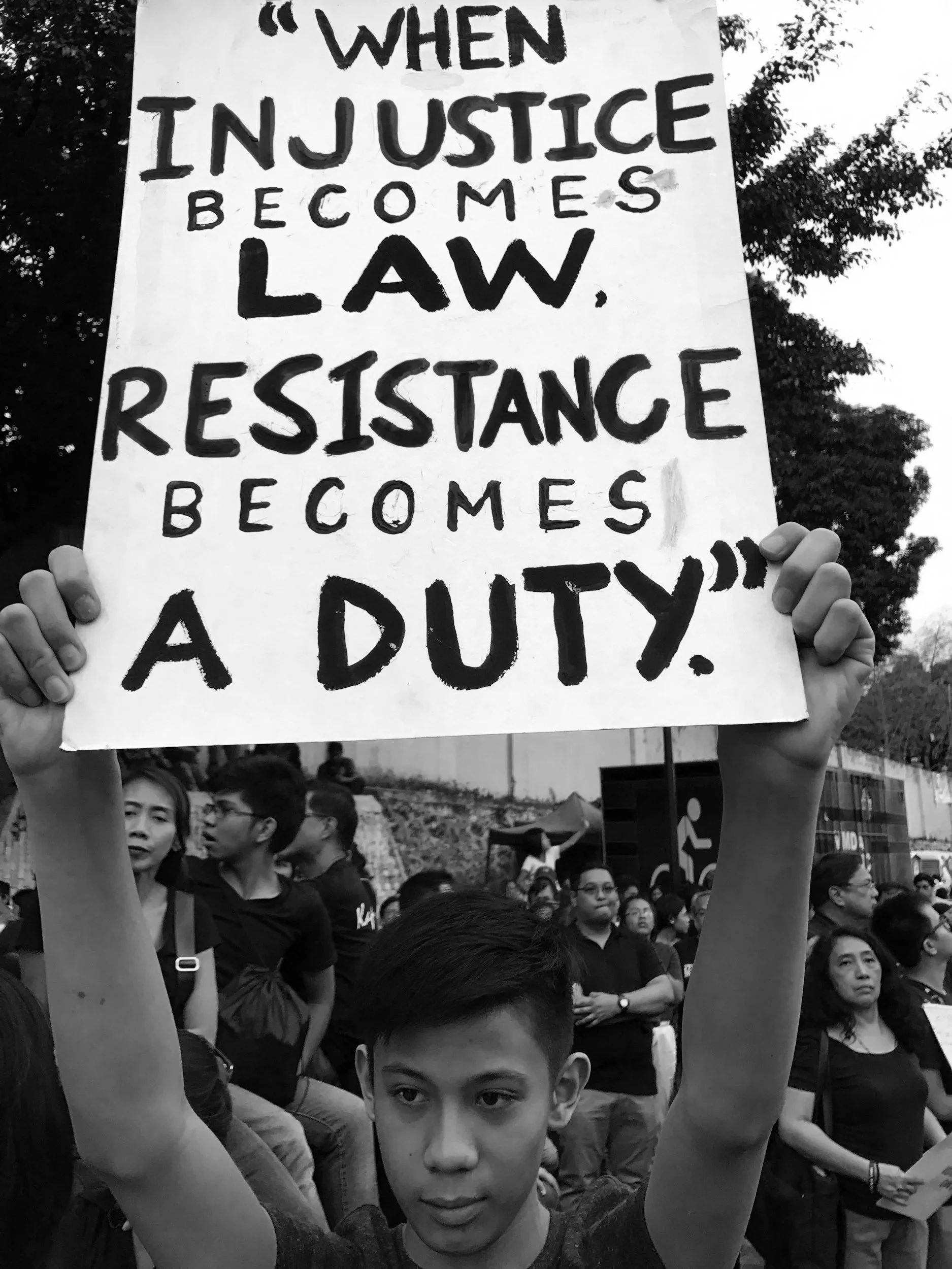 Crowd of people protesting, with a person holding a sign that reads: 'When in justice becomes law, resistance becomes a duty.'