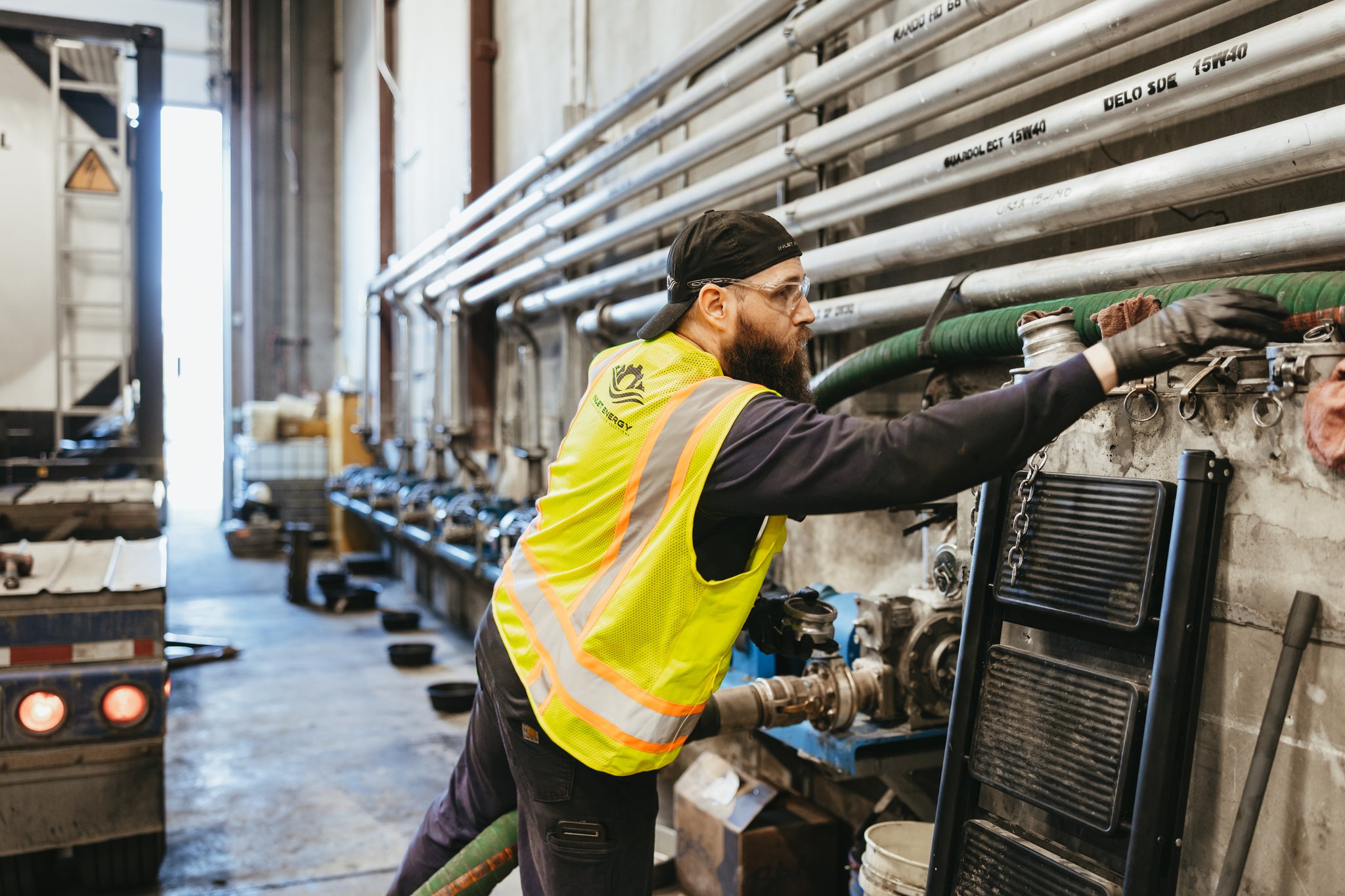 Man wearing safety glasses and a high-visibility vest working on industrial equipment in a factory or warehouse.