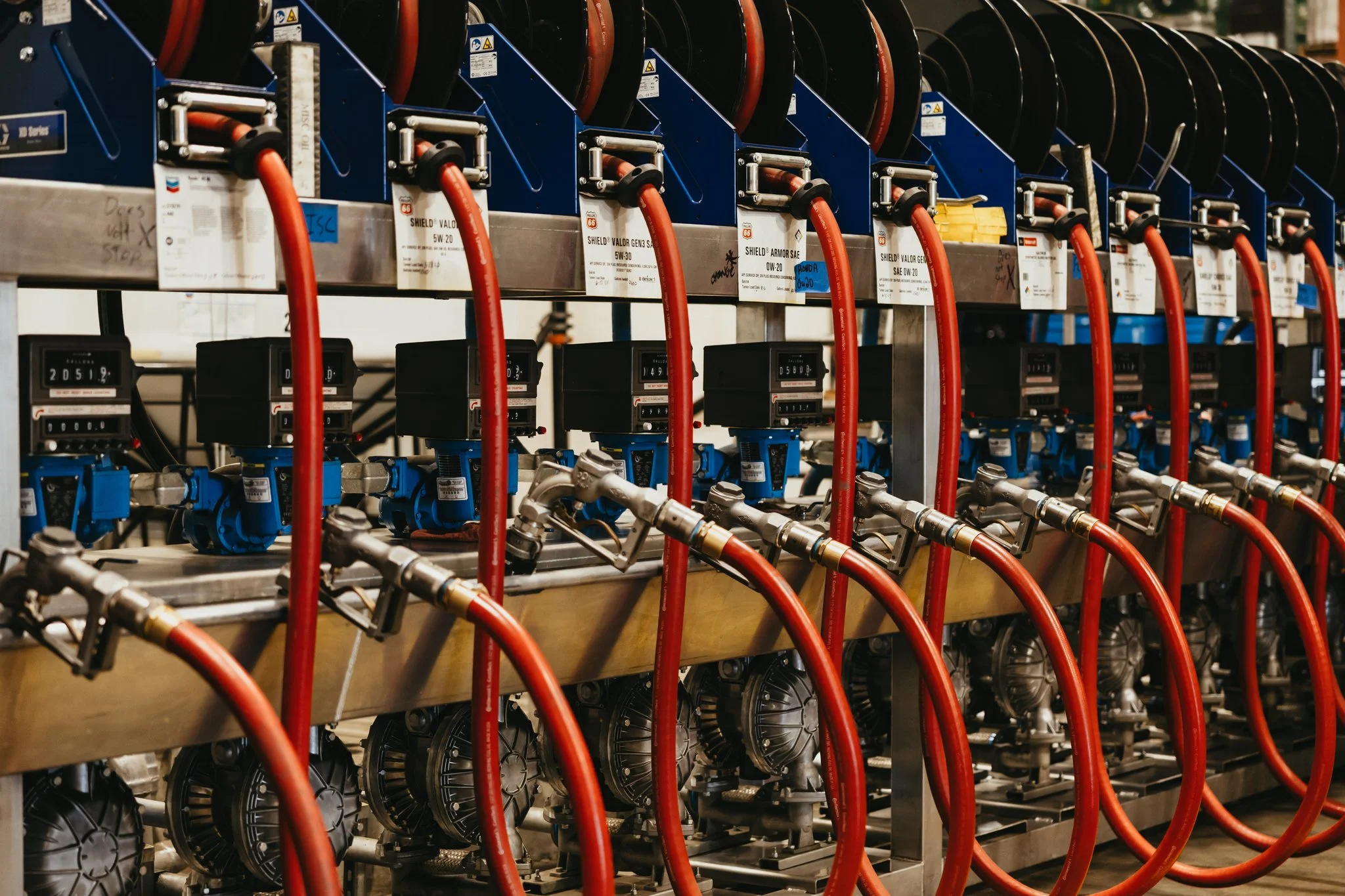 Industrial equipment with pipes and gauges arranged in rows, with red hoses connected to each piece of machinery.