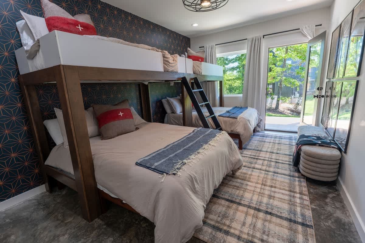 Bedroom with a bunk bed, patterned wallpaper, and a view of greenery outside through large windows.