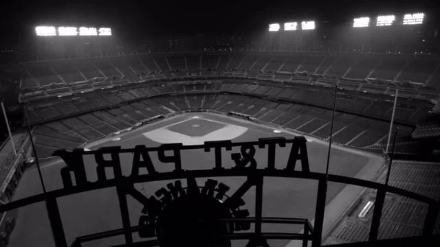 Empty baseball stadium at night with view from behind home plate, view of the field and seating areas.