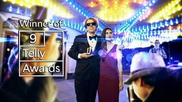 Two people dressed formally holding an award at the 9 Telly Awards ceremony, with colorful string lights overhead and other attendees in the background.