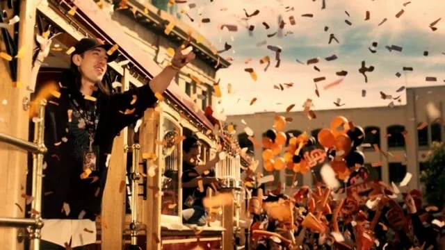 Person on a parade float throwing confetti during a celebration, with balloons in the background.