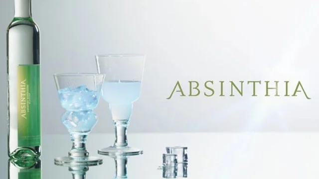A bottle of Absinthe, two glasses with one filled with ice and the other with clear liquid, and a few small round objects with the word 'Absinthe' in green text in the background.