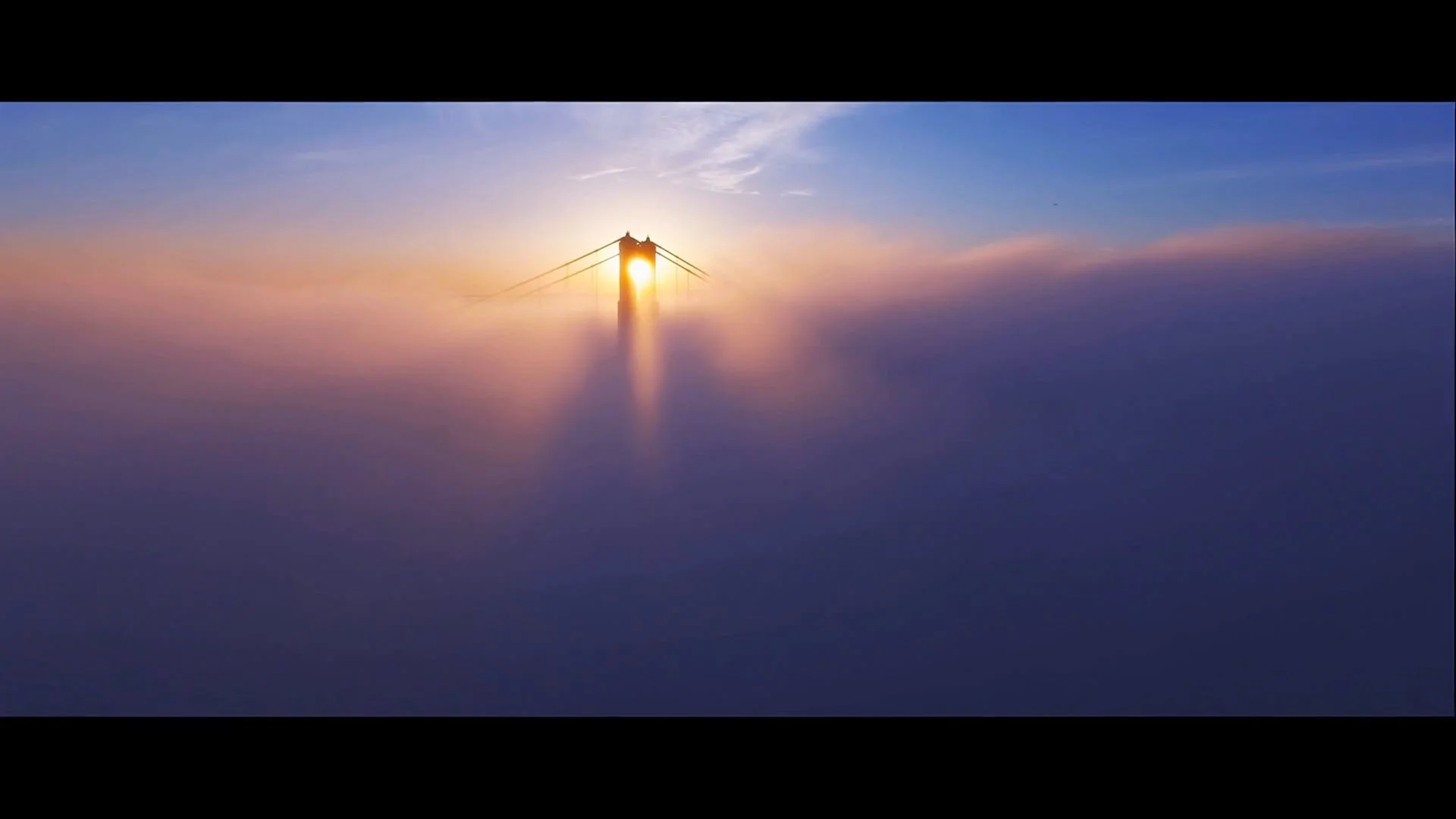Sunset behind a suspension bridge with fog or clouds at the horizon