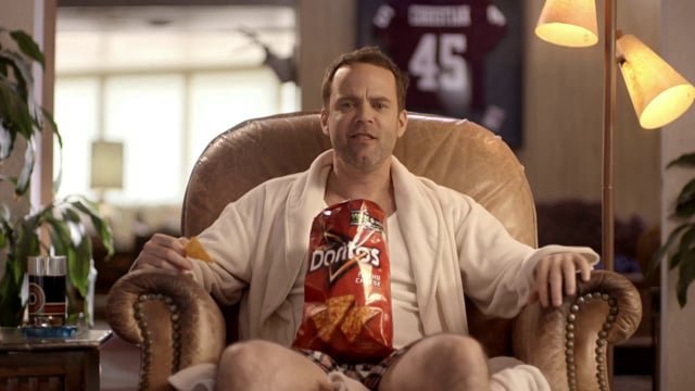 A man sitting in a recliner with a bag of Doritos chips resting on his chest.