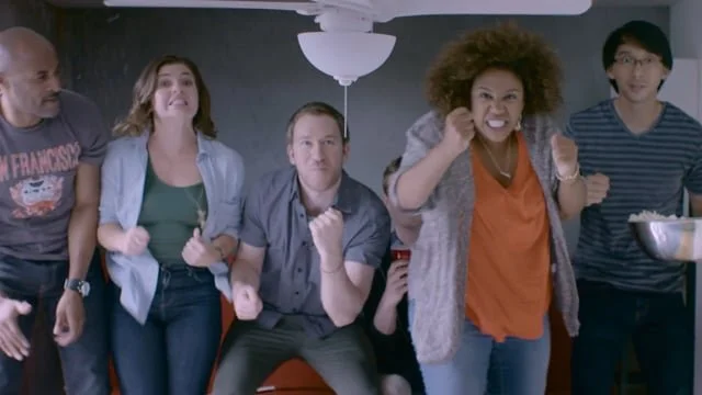 Group of five people watching a sports game, showing excitement and frustration.