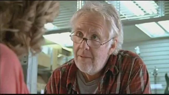 A man with glasses and a beard talking to a woman with curly hair at a store counter.