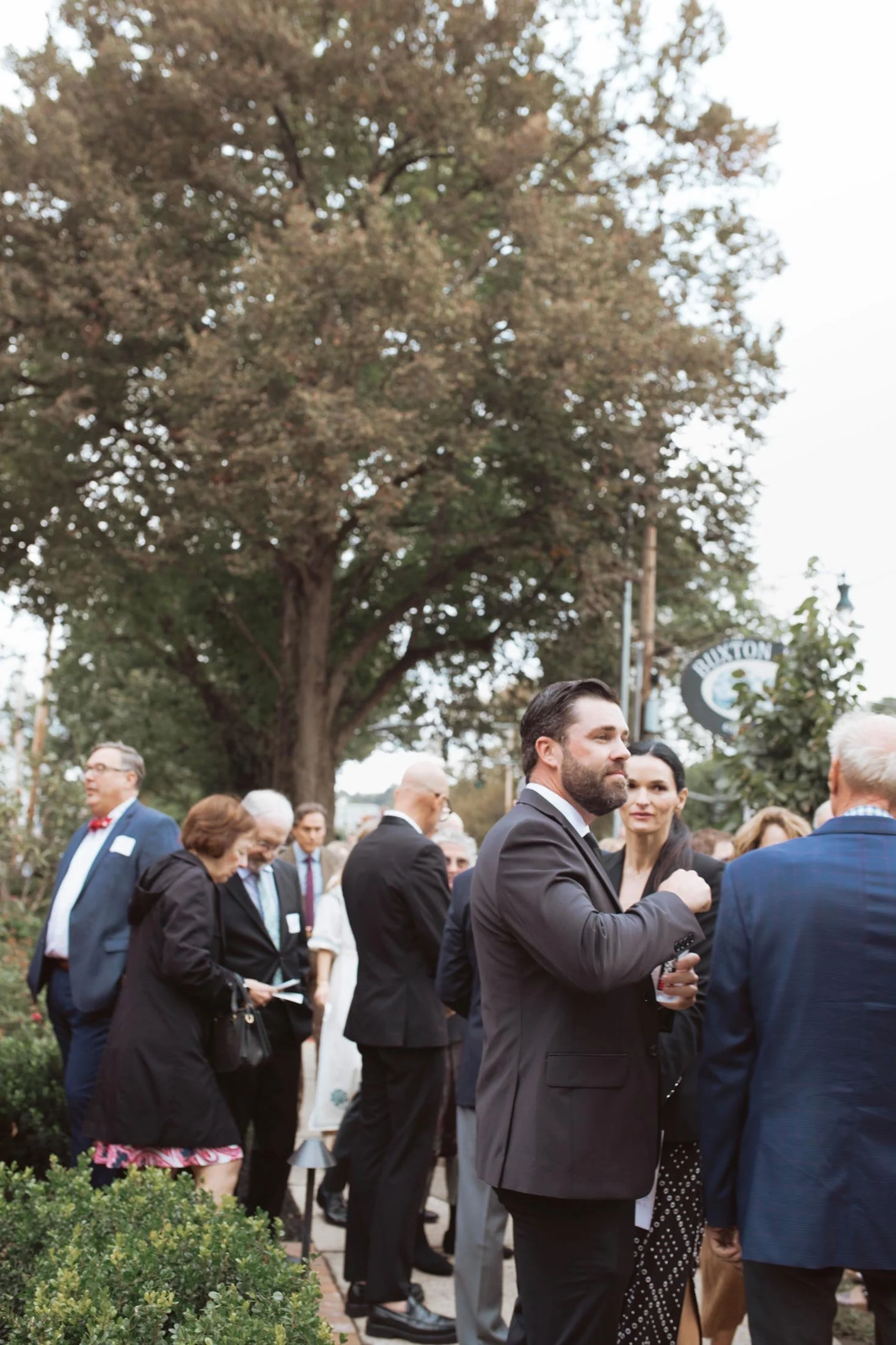 Guests chatting beneath the trees at the celebration.
